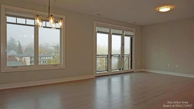 spare room featuring a wealth of natural light, hardwood / wood-style floors, and a notable chandelier