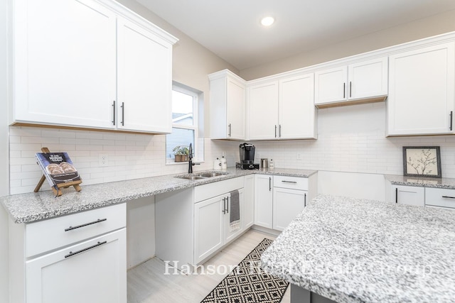 kitchen with white cabinets, backsplash, light stone countertops, and sink