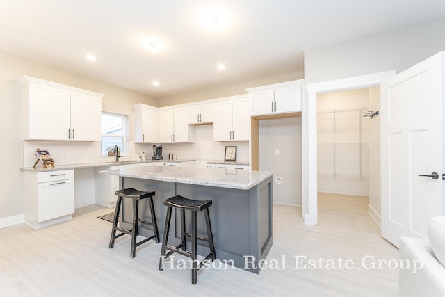 kitchen with a breakfast bar, decorative backsplash, white cabinetry, and a kitchen island