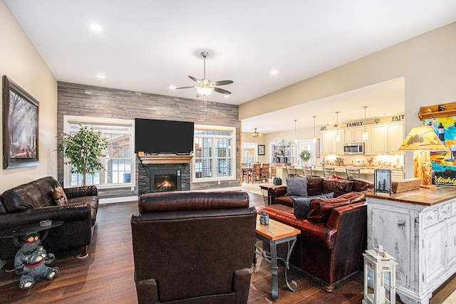 living room featuring dark hardwood / wood-style floors, a stone fireplace, and ceiling fan