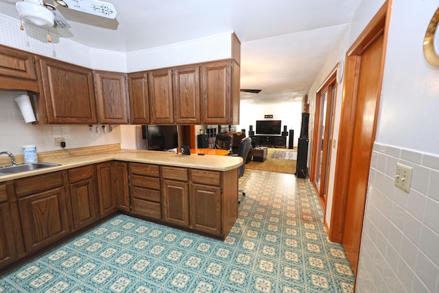 kitchen featuring sink, kitchen peninsula, ceiling fan, and tile walls