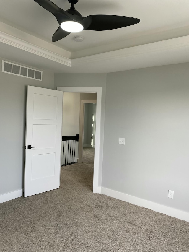 spare room with ceiling fan, a raised ceiling, and carpet floors