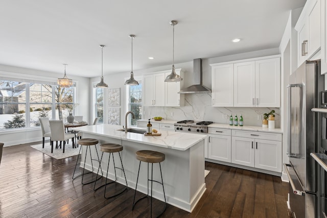 kitchen with appliances with stainless steel finishes, decorative light fixtures, white cabinets, and wall chimney exhaust hood