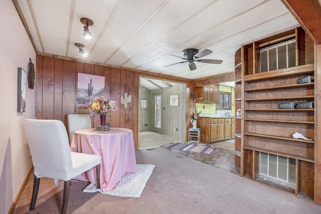 carpeted dining space featuring ceiling fan and wood walls