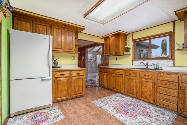 kitchen with light wood-type flooring, white fridge, and sink