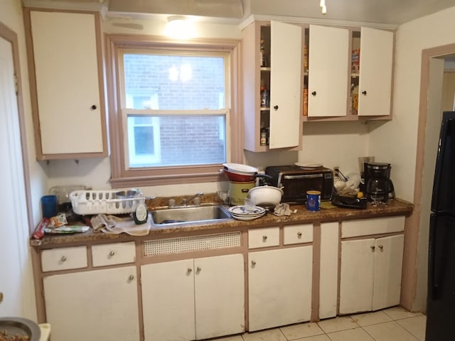 kitchen featuring black refrigerator, white cabinetry, sink, and light tile patterned floors