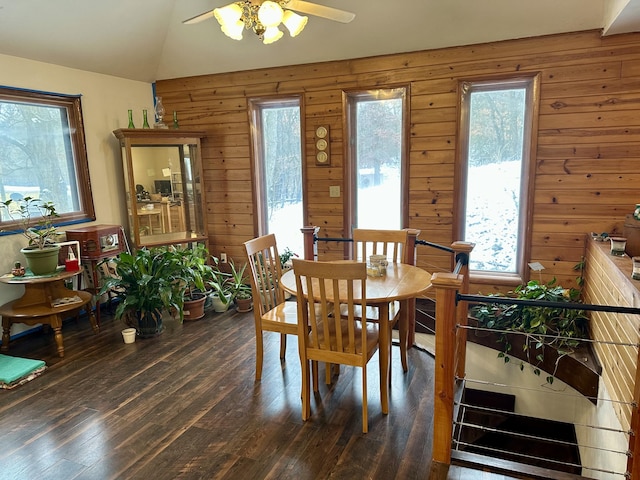 dining space featuring wood walls, ceiling fan, dark wood-type flooring, and lofted ceiling