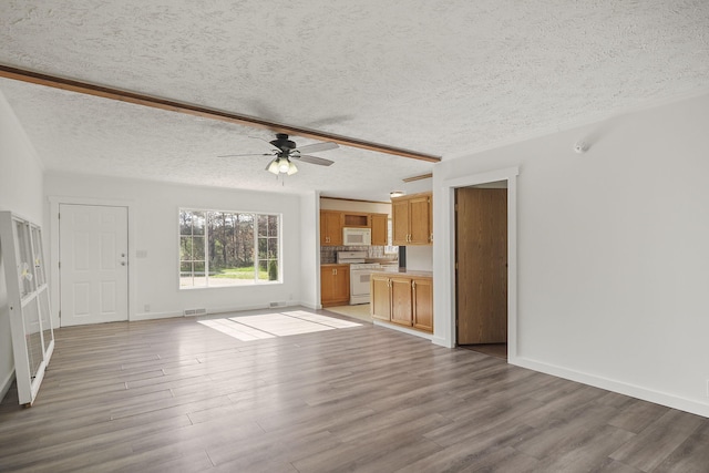 unfurnished living room featuring beam ceiling, a textured ceiling, light hardwood / wood-style floors, and ceiling fan