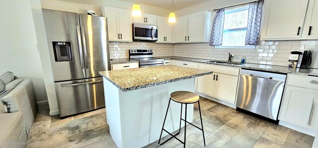 kitchen with appliances with stainless steel finishes, sink, white cabinets, a center island, and hanging light fixtures