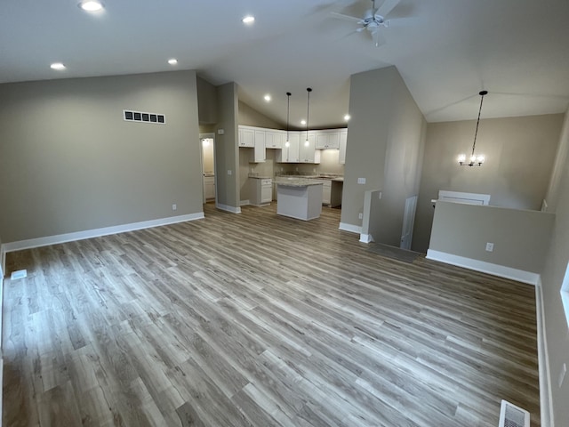 unfurnished living room with ceiling fan with notable chandelier, wood finished floors, visible vents, and baseboards