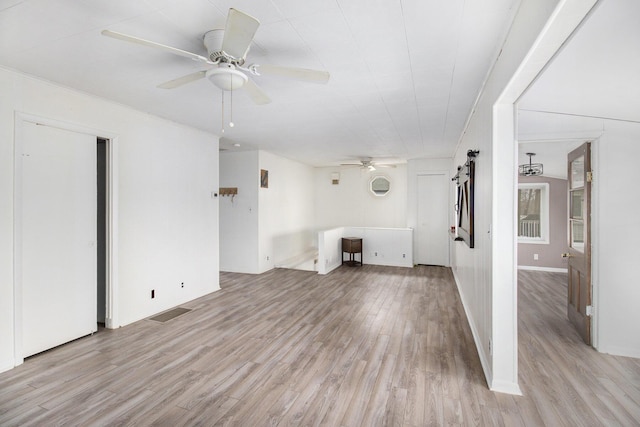 unfurnished living room featuring a barn door, ceiling fan, and light hardwood / wood-style flooring