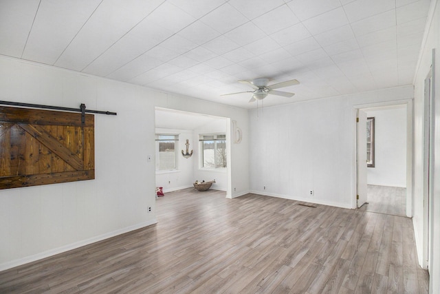 unfurnished living room with ceiling fan, a barn door, and light hardwood / wood-style flooring