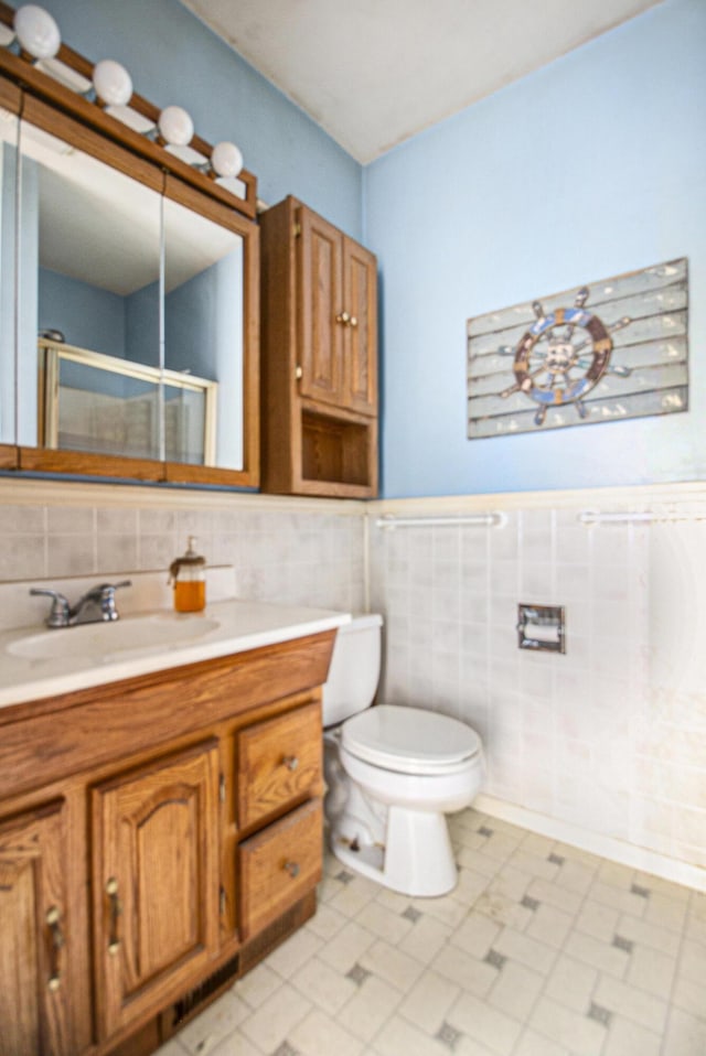 bathroom with vanity, a shower with shower door, tile walls, and toilet