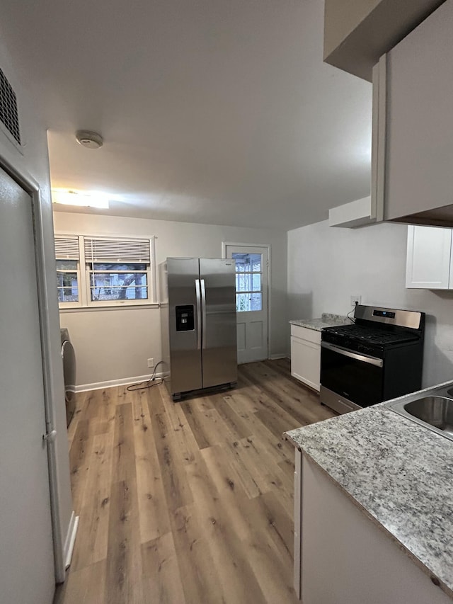 kitchen with white cabinets, sink, light stone countertops, appliances with stainless steel finishes, and light hardwood / wood-style floors