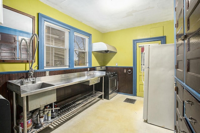 kitchen with black range with gas cooktop, stainless steel counters, sink, white refrigerator, and wood walls