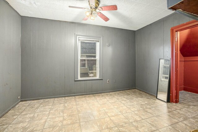 spare room with ceiling fan and wood walls