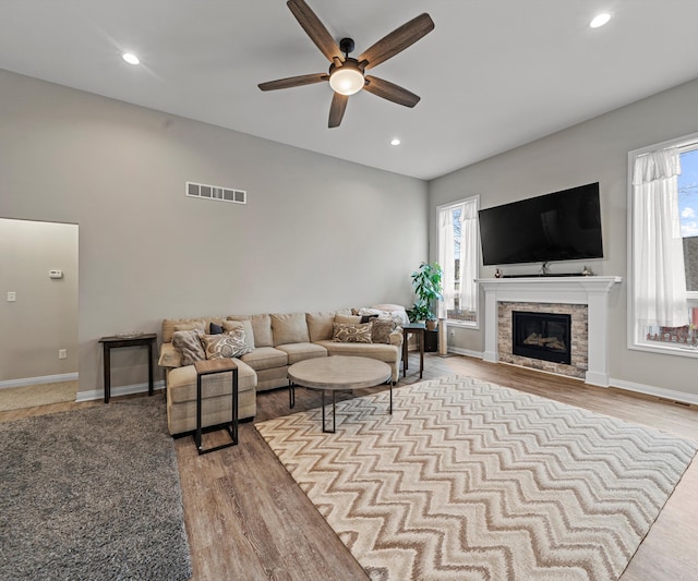 living room with a tiled fireplace, ceiling fan, and light wood-type flooring