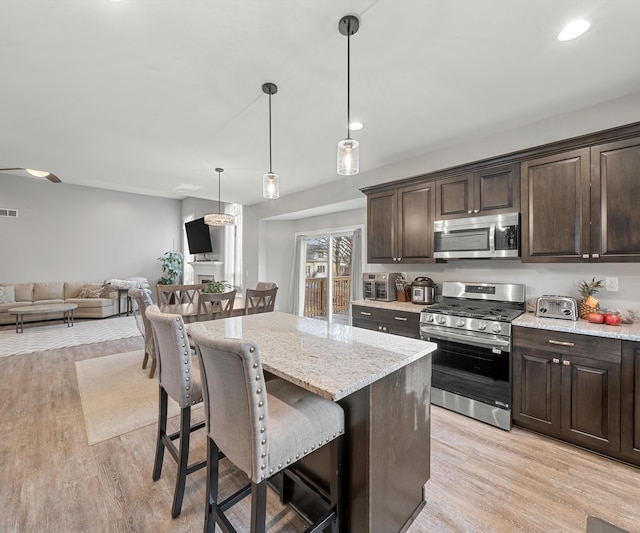 kitchen featuring hanging light fixtures, dark brown cabinets, a breakfast bar, and appliances with stainless steel finishes