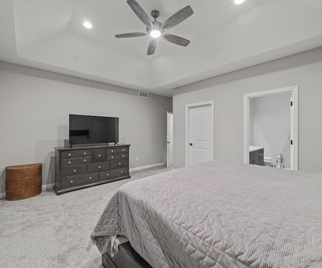 carpeted bedroom featuring a raised ceiling, ceiling fan, and ensuite bathroom