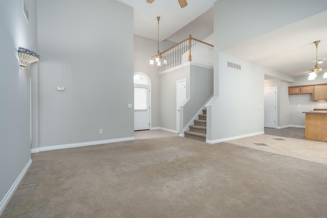 unfurnished living room featuring light carpet, a high ceiling, and ceiling fan with notable chandelier