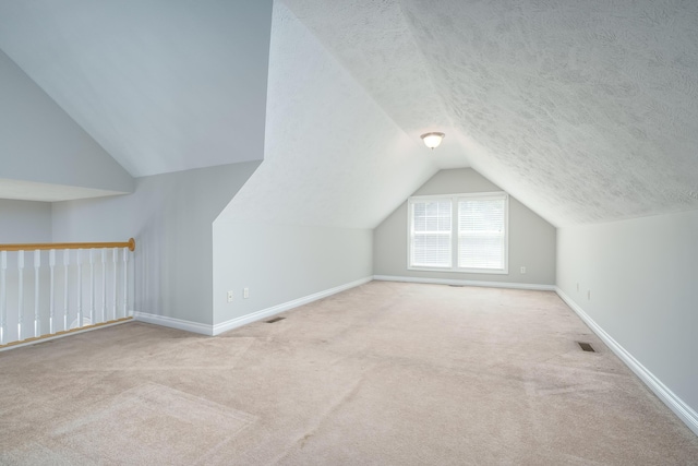 additional living space with a textured ceiling, light colored carpet, and lofted ceiling