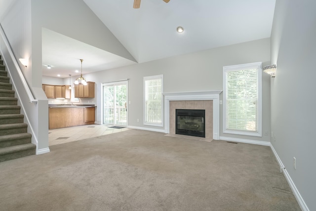 unfurnished living room featuring a fireplace, light carpet, ceiling fan with notable chandelier, and high vaulted ceiling