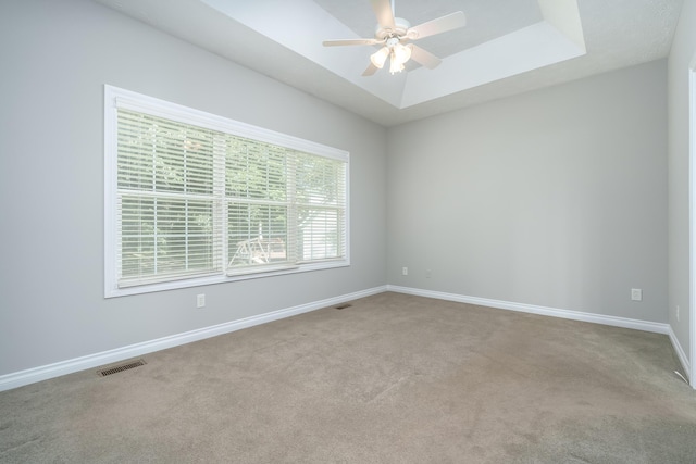 carpeted empty room with ceiling fan and a tray ceiling