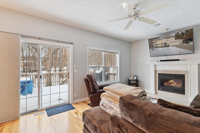 living room featuring a textured ceiling, light hardwood / wood-style flooring, ceiling fan, and a tiled fireplace