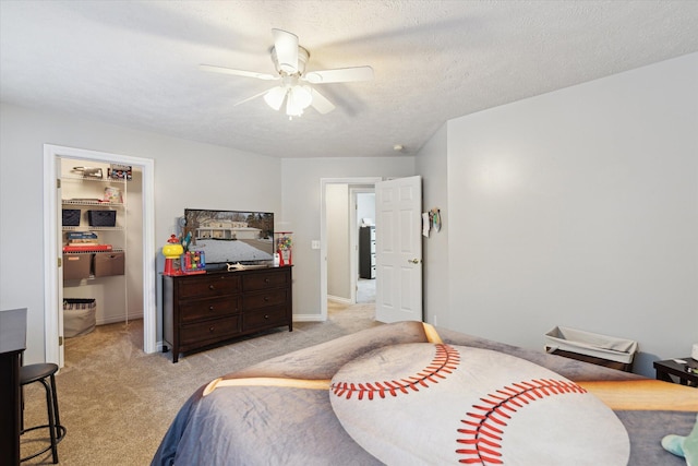 bedroom featuring a textured ceiling, a walk in closet, light colored carpet, and ceiling fan