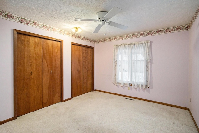 unfurnished bedroom featuring ceiling fan, carpet floors, a textured ceiling, and multiple closets