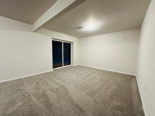 carpeted empty room featuring beamed ceiling and a textured ceiling