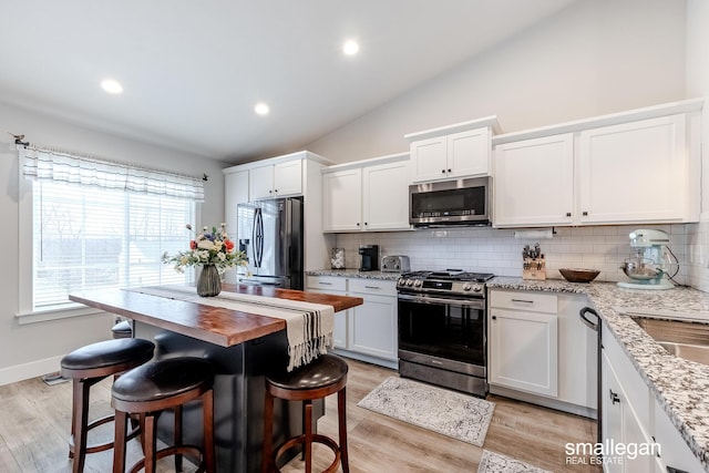 kitchen with light stone countertops, appliances with stainless steel finishes, white cabinets, light hardwood / wood-style floors, and lofted ceiling