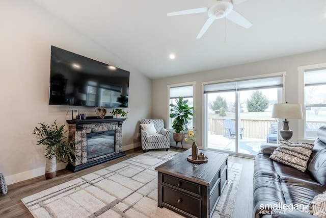 living room featuring ceiling fan, a fireplace, lofted ceiling, and light wood-type flooring