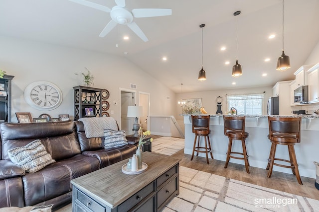 living room with ceiling fan with notable chandelier, vaulted ceiling, and light hardwood / wood-style flooring