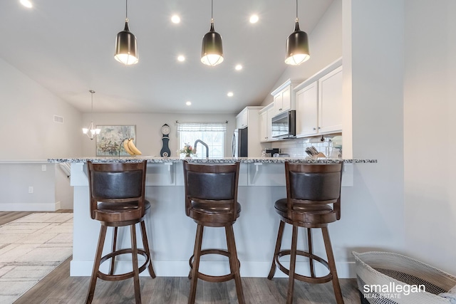 kitchen with tasteful backsplash, white cabinetry, a breakfast bar, and lofted ceiling