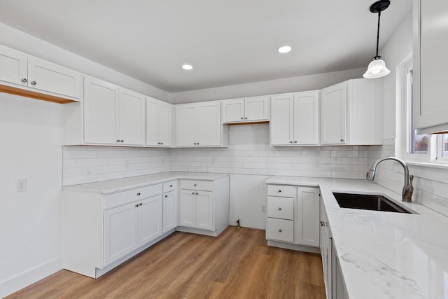 kitchen featuring backsplash, sink, light hardwood / wood-style flooring, white cabinetry, and hanging light fixtures