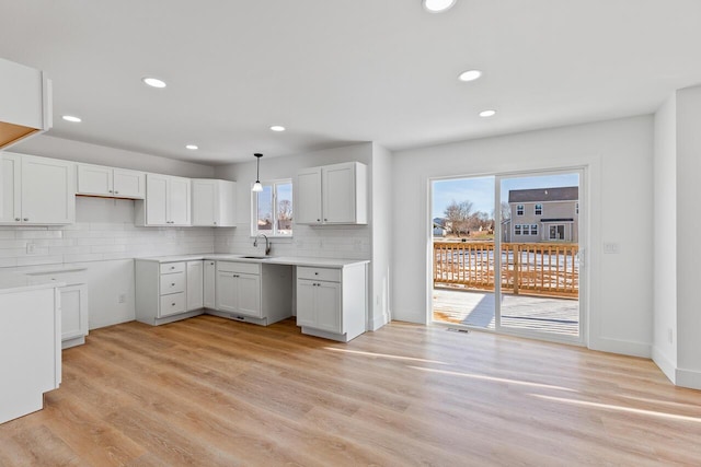 kitchen with decorative backsplash, light hardwood / wood-style flooring, white cabinetry, and hanging light fixtures