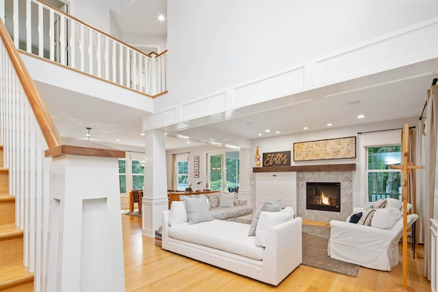 living room with a tile fireplace, a high ceiling, decorative columns, and light hardwood / wood-style flooring