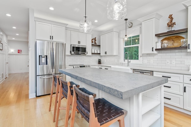 kitchen featuring white cabinets, hanging light fixtures, a kitchen island, a kitchen bar, and stainless steel appliances