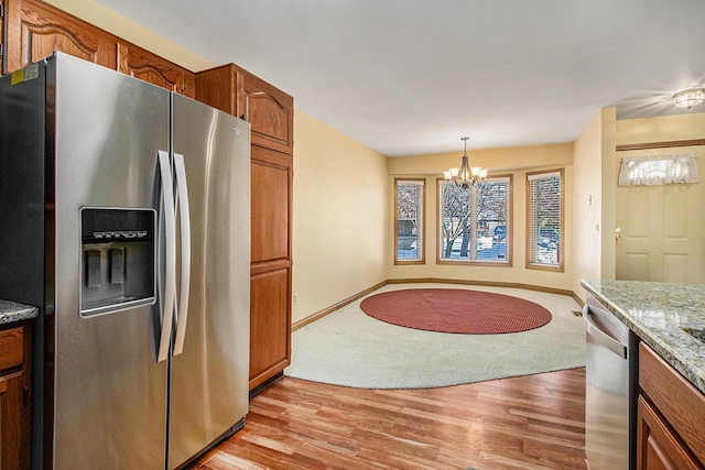 kitchen with appliances with stainless steel finishes, hanging light fixtures, a notable chandelier, light stone countertops, and light wood-type flooring