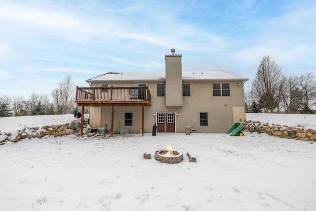 snow covered rear of property featuring a wooden deck, cooling unit, and a fire pit