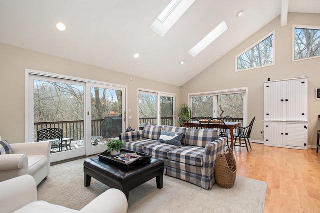 living room with light hardwood / wood-style floors, high vaulted ceiling, and a skylight