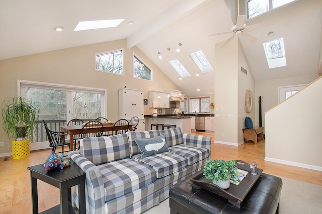 living room with a towering ceiling, light wood-type flooring, ceiling fan, and beam ceiling