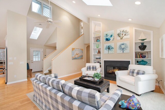 living room featuring light hardwood / wood-style floors, built in features, ceiling fan, and vaulted ceiling with skylight