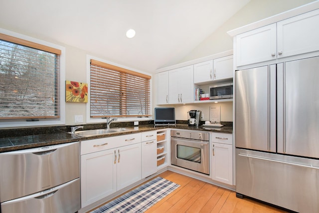 kitchen with appliances with stainless steel finishes, vaulted ceiling, sink, dark stone countertops, and white cabinetry