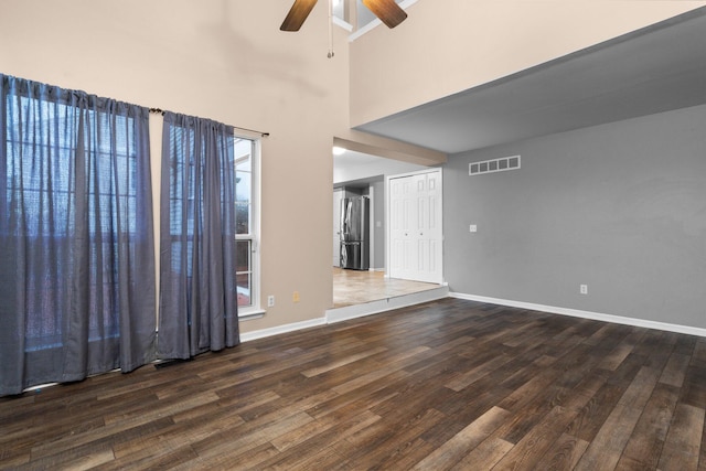 unfurnished living room featuring a high ceiling, ceiling fan, and dark wood-type flooring