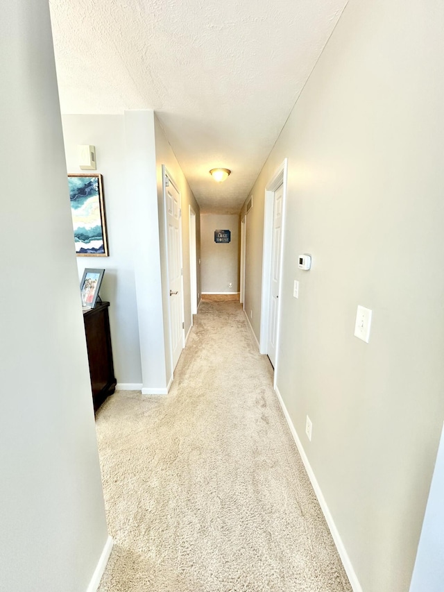 corridor with a textured ceiling and light carpet