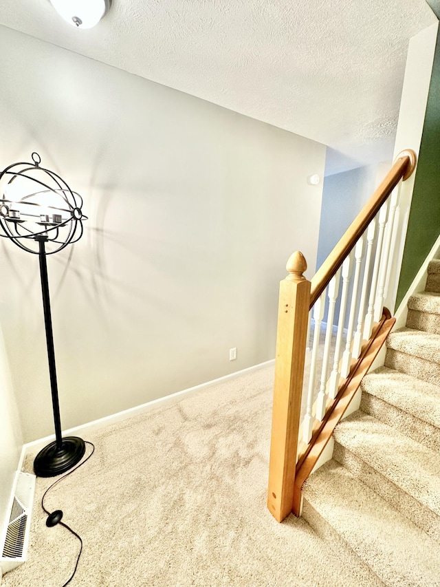 staircase featuring a textured ceiling and carpet floors