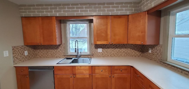 kitchen featuring brown cabinets, light countertops, decorative backsplash, stainless steel dishwasher, and a sink