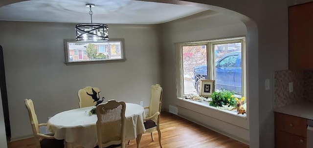 dining space with arched walkways, visible vents, light wood-style flooring, and an inviting chandelier